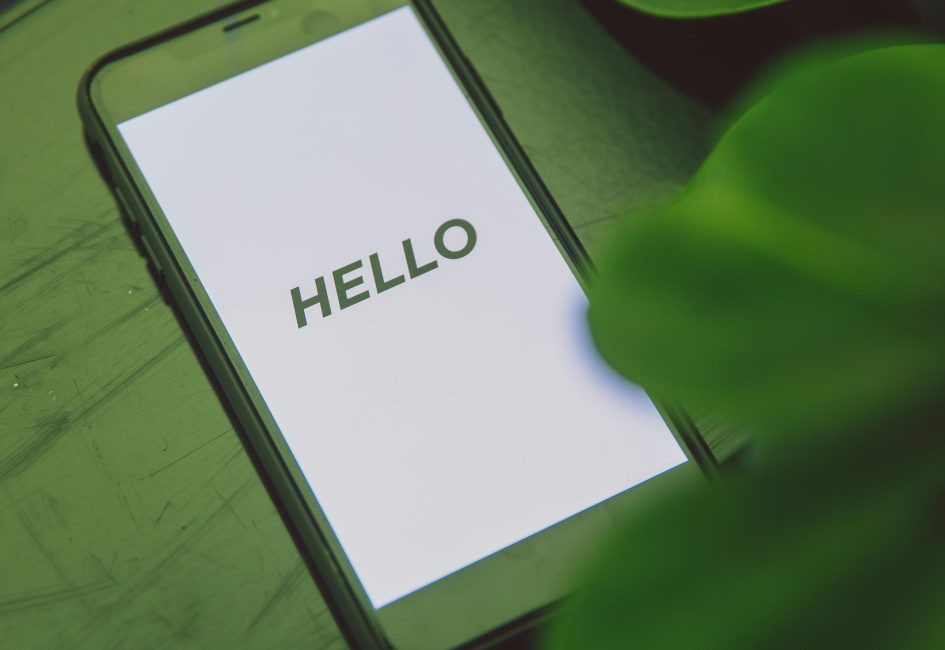 Close-up of a smartphone with 'Hello' text placed on a leafy green surface, emphasizing technology and nature.